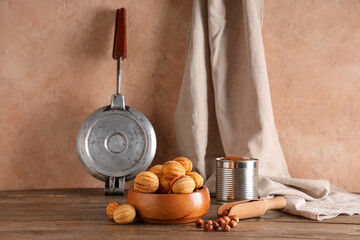 Bowl with tasty walnut shaped cookies, boiled condensed milk and hazelnuts on wooden table
