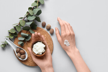 Female hands with cork cutting board, green twigs, shea butter and nuts on white background