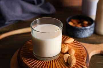 Glass of fresh almond milk and board with nuts on wooden background