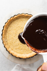 Overhead view of tart shell being filled with chocolate ganache, top view of chocolate filling in a baked pie shell, process of making chocolate tart