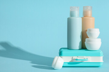 Travel cosmetic kit and mini suitcase on color background