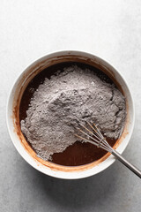 Overhead view of flour and cocoa powder being whisked into chocolate batter, process of making chocolate mud cake, making a dark chocolate cake