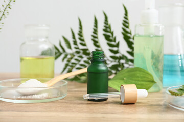 Laboratory glassware with ingredients and samples for preparing natural cosmetics on brown wooden table near white wall