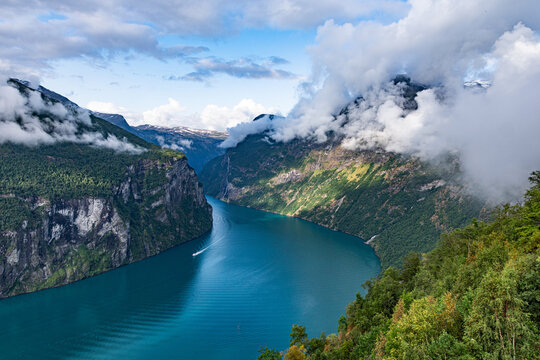 Fjord vista: boat glides through mountains and clouds.