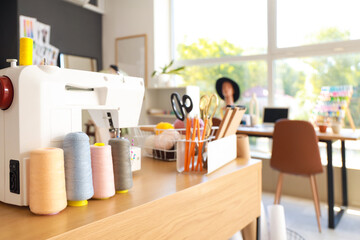 Sewing machine with thread spools on fashion designer's table in studio, closeup