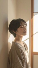 Serene Woman with Short Dark Hair Resting Against Wall in Sunlit Room