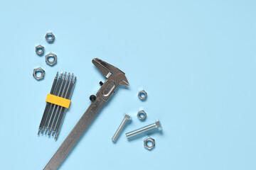 Caliper with screwdriver bits, tap bolts and chrome nuts on blue background