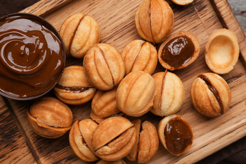 Cutting board of sweet walnut shaped cookies with boiled condensed milk on wooden background, closeup