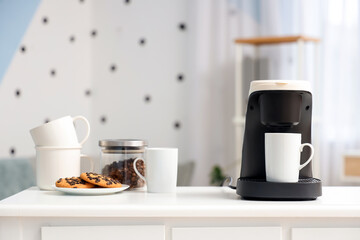 Coffee machine with cups, cookies and beans on table in office