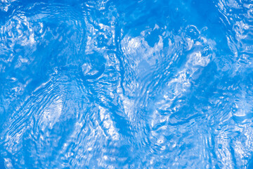 Blue water with ripples on the surface. Defocus blurred transparent blue colored clear calm water surface texture with splashes and bubbles. Water waves with shining pattern texture background.