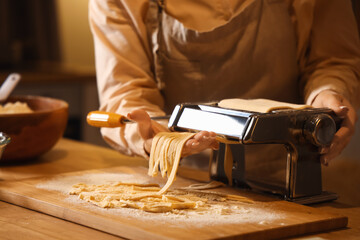 Young woman making pasta with machine at table in dark kitchen, closeup