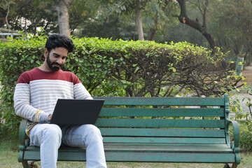 Fototapeta premium Happy indian man working on laptop at park