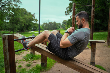 Man working out outdoors in the park, doing sit-ups on incline bench