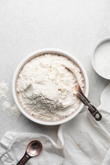 overhead view of All purpose flour with spoon on a granite countertop, top view of baking flour on a white countertop