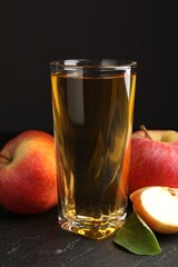 Fresh cider in glass, apples and green leaf on black table, closeup