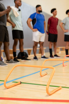Diverse male team standing in gym court behind orange agility hurdles preparing for drill