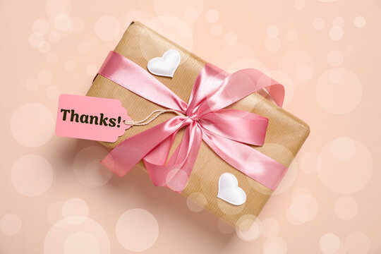 Thanks tag attached to gift box on dark beige background. Bokeh effect