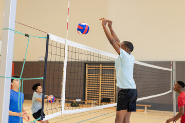 Diverse male team practicing volleyball drill at gym using net, red-blue volleyballs, copy space