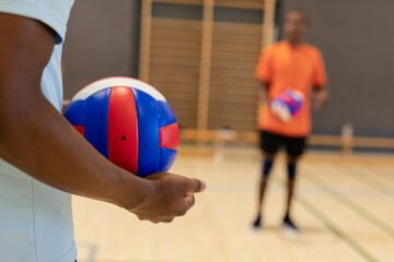 African american male partners practicing serve on gym court with volleyball, copy space