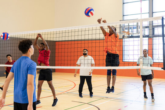 African american man jumping, blocking volleyball at net during match inside gym
