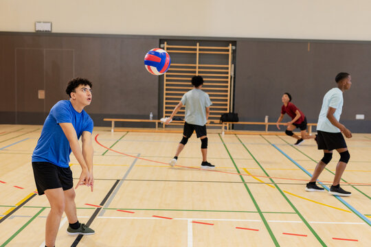 Diverse male partners playing volleyball on gymnasium court with bench and wall bars, copy space