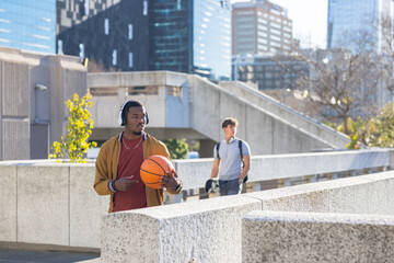 Diverse male students walking along elevated concrete plaza walkway holding basketball, backpack