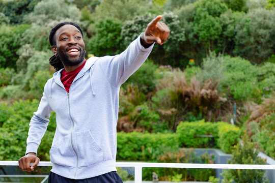 African American man standing on balcony by white railing overlooking garden slope, pointing right