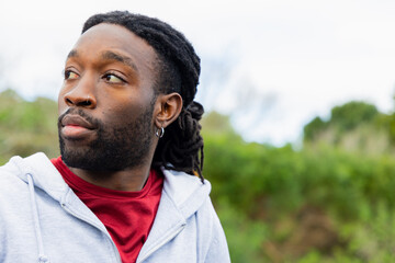 Adult African American man gazing left in park with nose ring and hoop earring, copy space