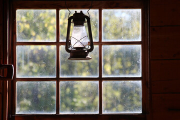vintage hurricane lantern in silhouette against a multi paned dirty glass window showing against a green leaf backdrop