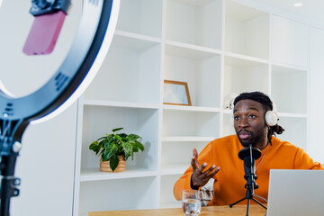 African American man speaking into microphone in home office with ring light and laptop, copy space