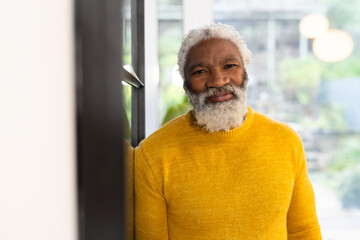 Senior African American man leaning against window wearing sweater, gazing at pendants, copy space