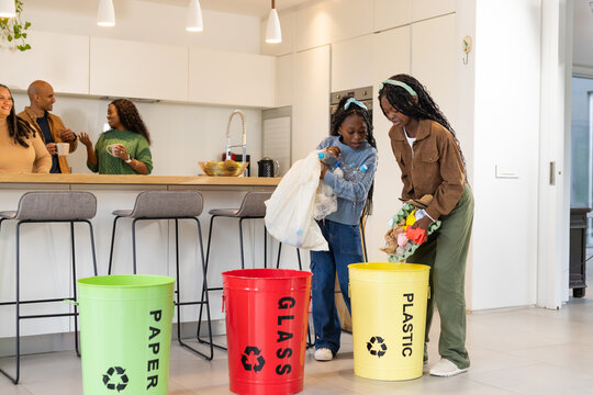 Two African American girls sorting recyclables into color-coded bins at kitchen island, copy space