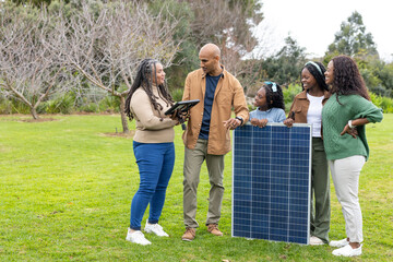 Diverse family consulting solar technician while examining solar panel and tablet on green lawn