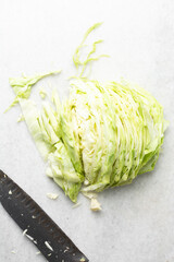Overhead view of sliced cabbage on a marble countertop, top view of cabbage leaves being shredded, green cabbage being sliced