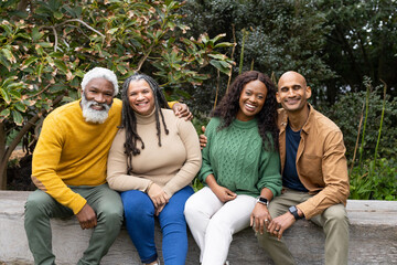 Senior couple and African American couple sitting on wooden bench in garden surrounded by foliage