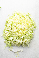 Overhead view of sliced cabbage on a marble countertop, top view of cabbage leaves being shredded, green cabbage being sliced