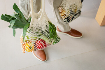 African American man standing on gray tile floor holding off-white mesh bags filled with produce