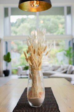 Clear glass vase is displaying dried grasses and citrus slices on table runner under filament lamp