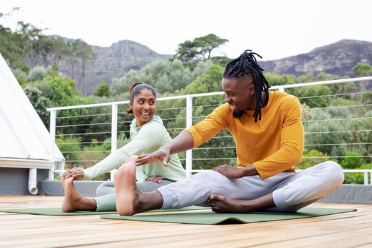 Diverse friends stretching hamstrings on rooftop terrace in sportswear on green yoga mats