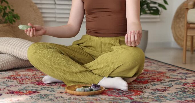 Woman with beautiful fluorite gemstone meditating on floor indoors, closeup