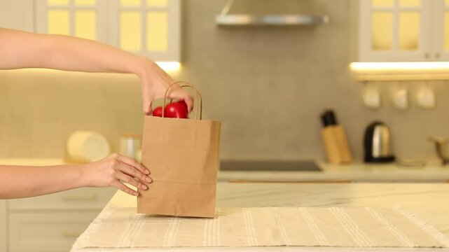 Packaging. Woman taking zucchini and bell pepper out of paper bag at table in kitchen, closeup