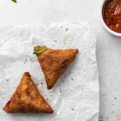 Overhead view of samosa with dip on parchment paper, top view of beef samosa on a white background