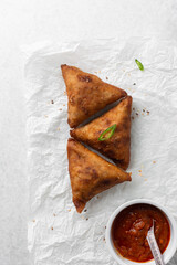Overhead view of samosa with dip on parchment paper, top view of beef samosa on a white background