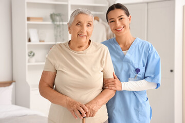 Fototapeta premium Female caregiver and happy senior woman with walking stick at home