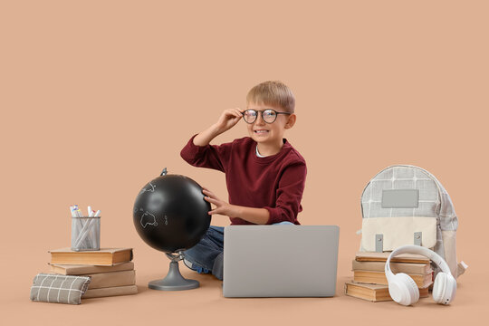 Little schoolboy with globe and laptop studying on beige background - Powered by Adobe