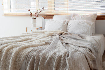 Comfortable bed and vase with cotton flowers on bedside table near window in bedroom, closeup