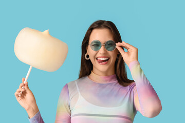 Beautiful young happy woman in sunglasses with cotton candy on blue background