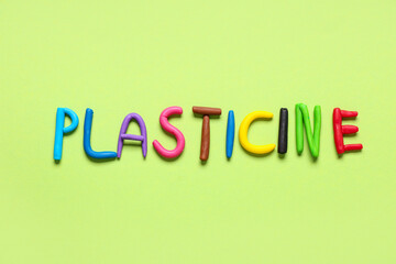 Word PLASTICINE made of play dough on green background