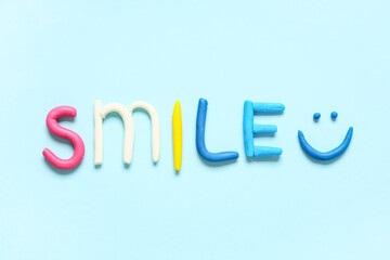 Word SMILE made of play dough on light blue background
