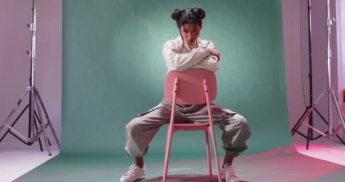 Young woman in studio sitting on chair confidently, wearing casual streetwear